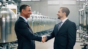 Two Businessmen shake hands on a deal with view Background of large brewery brewing plant video