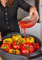 A woman puts tomato paste into stuffed peppers with a mixture of rice, lentils and vegetables in a frying pan on an induction hob in her home kitchen photo