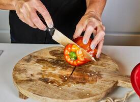Close-up of hands slicing a red bell pepper on a wooden cutting board, showcasing cooking preparation and fresh ingredients. photo