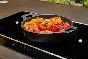 Stuffed peppers with a mixture of rice, lentils and vegetables in a frying pan on an induction cooker in a home kitchen photo