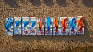 Top view of pedal boats along the beach with the sea. Aerial view of Mediterranean beach with sand and umbrellas. Colorful summer background expressing relaxation, summer vibes, sea, vacation, travel. photo