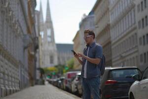 A man using smartphone wearing white sunglasses and gray backpack on the street in Vienna on a hot sunny summer day. Tourism and sightseeing concept photo