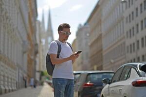 A man using smartphone wearing white sunglasses and gray backpack on the street in Vienna on a hot sunny summer day. Tourism and sightseeing concept photo