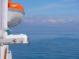 Lifeboat on the deck of a ferry cruise ship. Saving lives on the water concept. Side view against the background of the sky and calm sea in sunny weather. photo