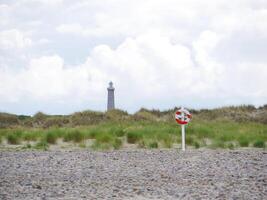 Red and white lifebuoy on the beach in Skagen, Denmark at the background of a lighthouse. Life saving rescue buoy. Lifeguard preserving concept photo