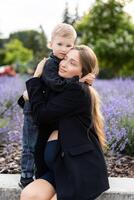 Pregnant mother and her little son spending time together in the park, hugging and smiling. photo