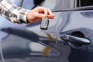 Emotional guy holding key in hand and smiling at camera. Man showing key from his new electric car. Young man buying auto at dealership salon photo