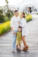 Man and woman walking down with their son wooden walkway, surrounded by trees and nature. They are strolling along the path in a leisurely manner photo
