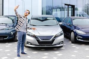 Happy man taking selfie through smart phone after purchasing new car. The man showing the purchased car via link over the phone photo