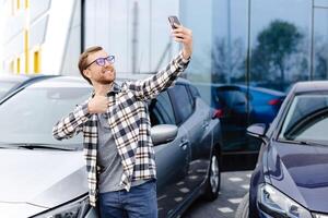 Happy man taking selfie through smart phone after purchasing new car. The man showing the purchased car via link over the phone photo