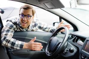 Young man looking through window inside new car, checking it before purchase at modern dealership store. Cheerful guy buying or renting automobile at showroom photo