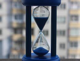 Closeup View Of Fallen Sand Inside Sandglass Over Defocused Facade Of Skyscraper On Background photo