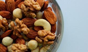 Detailed Photo Of Glass Bowl With Heap Of Variety Shelled Nuts At Side Of Image