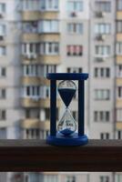 Blue Hourglass With Sand Falling Down On A Wooden Railing Of The Balcony Of A High Rise Building photo