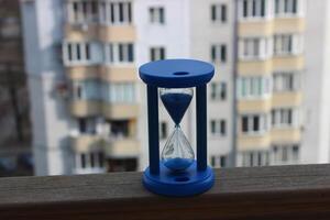 Falling blue sand in an hour glass with blurred residential apartments on background photo