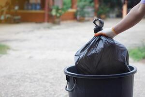 Hand holding garbage black bag putting in to the bin. Concept, garbage management, Keep clean for sanitary and community service for the best environment. Zero waste. photo