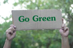 Hands hold paper card with text Go Green. Concept, environment conservation campaign. Campaign and motivate to do eco friendly activities for the earth. Protect nature. photo