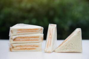 Homemade sandwich wrapped with transparent plastic in triangle shape, made from bread and stuff with mayonnaise and other filling stuffed. Ready to eat. Concept, simple food for meals. photo