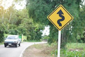 Yellow traffic sign with arrow left curve symbol beside the rural road to warn drivers to know the way ahead has left curve. Concept, Warning traffic sign for transportation. photo