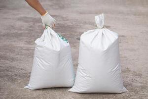 Close up man holds white polypropylene sack that contain full of agricultural grains, tied on the top with bamboo rope. Concept, reusable bag for contain crops, fertilizer or others. photo