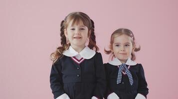 Two little girls dressed in school uniform, blank pink background photo