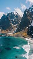 Snowy peaks rise above a turquoise ocean, with whitecaps crashing gently on the shore photo