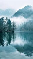 Misty morning over a still lake with forested mountain backdrop photo