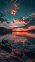 Sunset reflects on the calm water, with rocks in the foreground photo