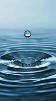 A single water droplet falls into still water, creating concentric ripples photo