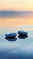 Two smooth stones sit gently on the surface of a calm ocean, reflecting the sunset sky photo