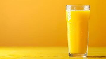 A tall glass of pineapple juice sits on a yellow table against a bright yellow background photo