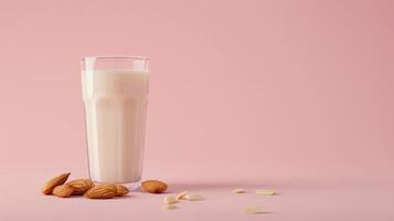 A glass of almond milk sits on a pink background with scattered almonds photo