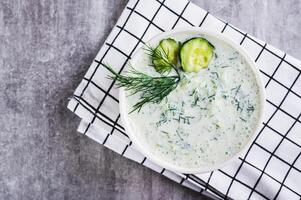 Close up of tzatziki sauce with cucumber, garlic and dill on kefir in a bowl on the table top view photo