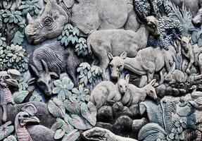 Jakarta, Indonesia - July 24th, 2024 - Rhino, komodo, and mousedeer wild animal pattern carving design isolated on horizontal stone wall background. photo