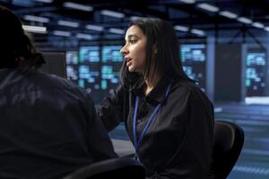 Indian woman in server hub ensuring data remains shielded from potential threats. Computer scientist and coworker safeguarding data center hardware against malicious access photo