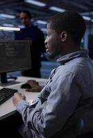 African american engineer in data center updating systems to keeps performance up and protect servers from exploitable software vulnerabilities. Worker looking for errors causing hardware to slow down photo
