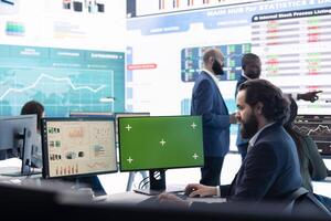 Business manager analyzes reports next to a green screen on pc, working with infographics and sales for development. Analyst consultant looks at isolated mockup display in office. photo