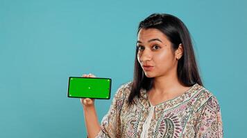 Smiling woman showing isolated screen mobile phone, doing promotion, studio background. Upbeat indian person holding copy space mockup cellphone used for advertising brands, camera B photo