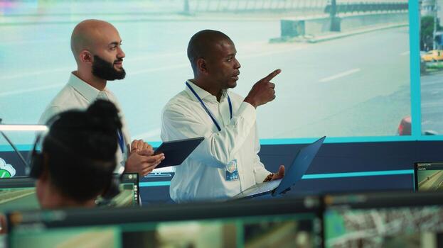 Diverse employees using CCTV surveillance system in monitoring traffic, tracking speed limits for public safety via satellite radar system. People operating on a big screen in control center. Camera A. photo