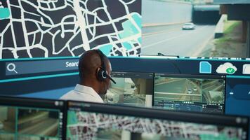 Operator uses satellite navigation map to guide delivery truck drivers, works in observation room to avoid traffic. African american employee tracing orders within the surveillance system. Camera B. photo
