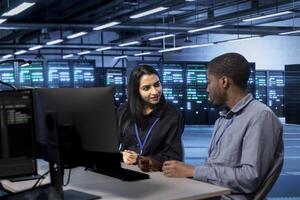 IT staff members using desktop PC to do maintenance in data center to extend equipment life span and avoid downtime. Teamworking colleagues monitoring blade servers for overheating problems photo
