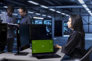 Computer scientist using green screen notebook to oversee blade servers used for managing databases. Woman working on mockup laptop in data center workspace storing information on rackmounts photo