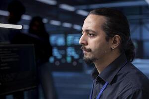 IT developer in data center updating systems to protect servers from exploitable software vulnerabilities. Close up shot of man looking for errors causing equipment to slow down photo