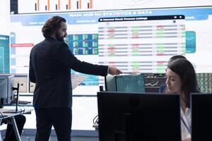 Financial manager briefing his team members about new corporation objectives, presenting their budget scheme with expenses. Resource allocation and project planning in control room. photo