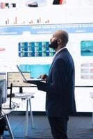 Administrative assistant examining important big data visualizations on a huge display, creating an analysis to review key performance indicators and business efficiency in office. photo