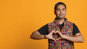 Portrait of smiling loving man doing heart symbol shape gesture with hands, showing kindness. Happy affectionate person doing tender love gesturing, isolated over studio background, camera A photo
