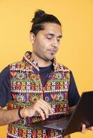 Indian man composing email, typing on laptop, frustrated with malfunctioning keyboard. Person sending mail online, struggling to use defective notebook, studio background photo