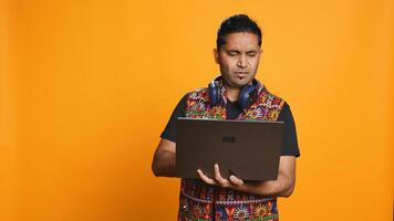 Indian man composing email, typing on laptop, frustrated with malfunctioning keyboard. Person sending mail online, struggling to use defective notebook, studio background, camera B photo