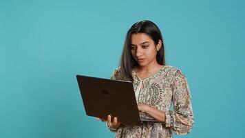 Indian woman composing email, typing on laptop, frustrated with malfunctioning keyboard. Person sending mail online, struggling to use defective notebook, studio background, camera A photo