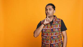Annoyed indian man doing shushing hand gesturing, irritated by noise, having negative mood. Person placing finger on lips, doing quiet sign gesture, studio background, camera B photo